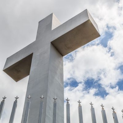 Mt. Helix cross with fence railing and a background of a cloudy blue sky in La Mesa, a city in San Diego, California.